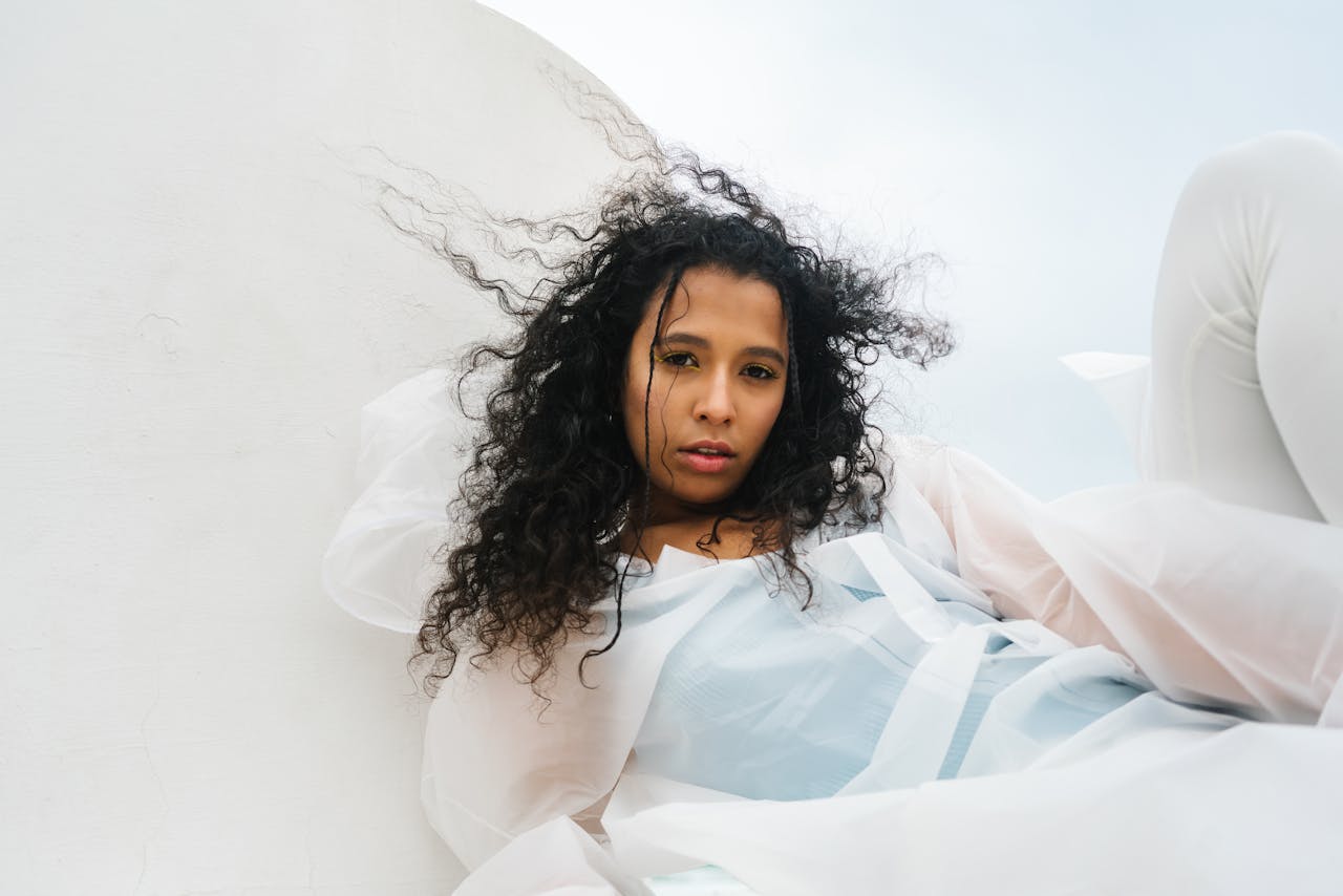 Artistic portrait of a woman with curly hair, wearing a white raincoat, captured from a unique angle.