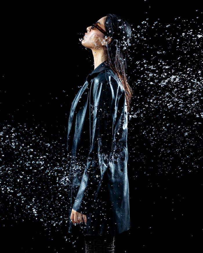 Model in a black coat posing with water splashes in a studio setup.